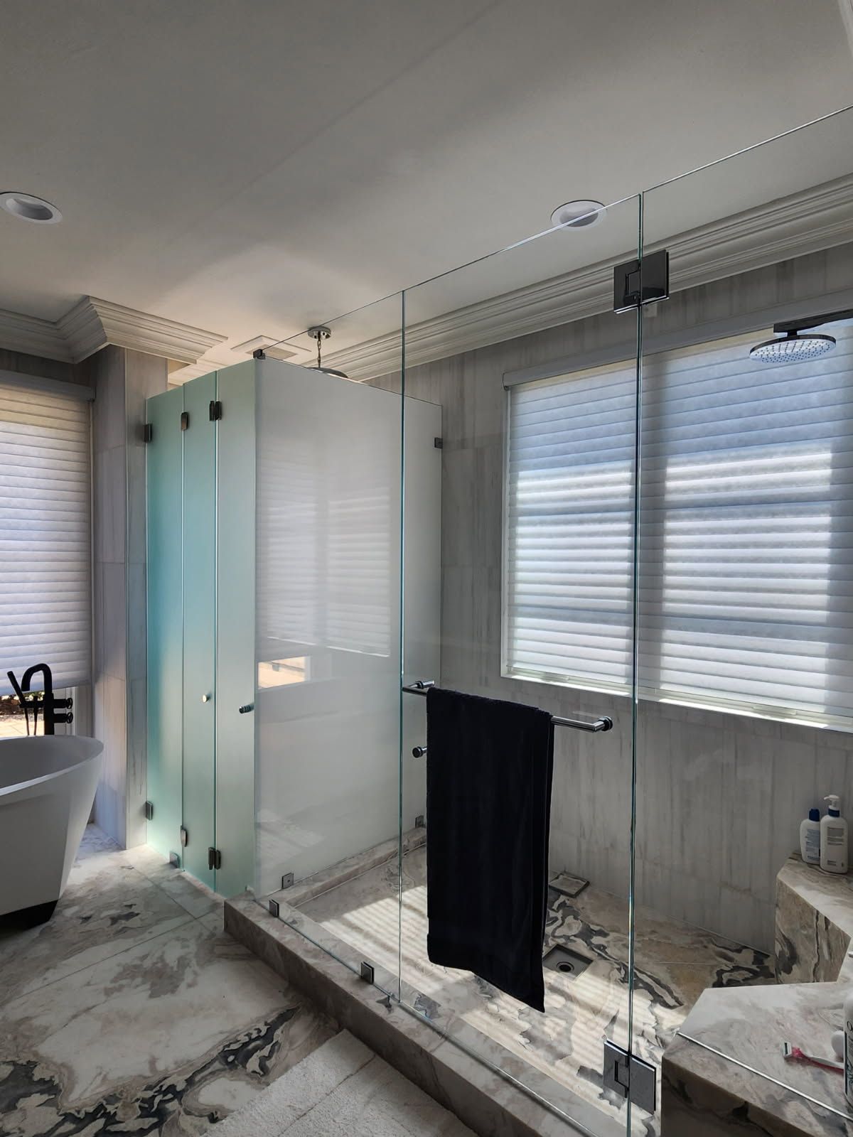 A modern bathroom with a glass shower enclosure and a window with blinds.