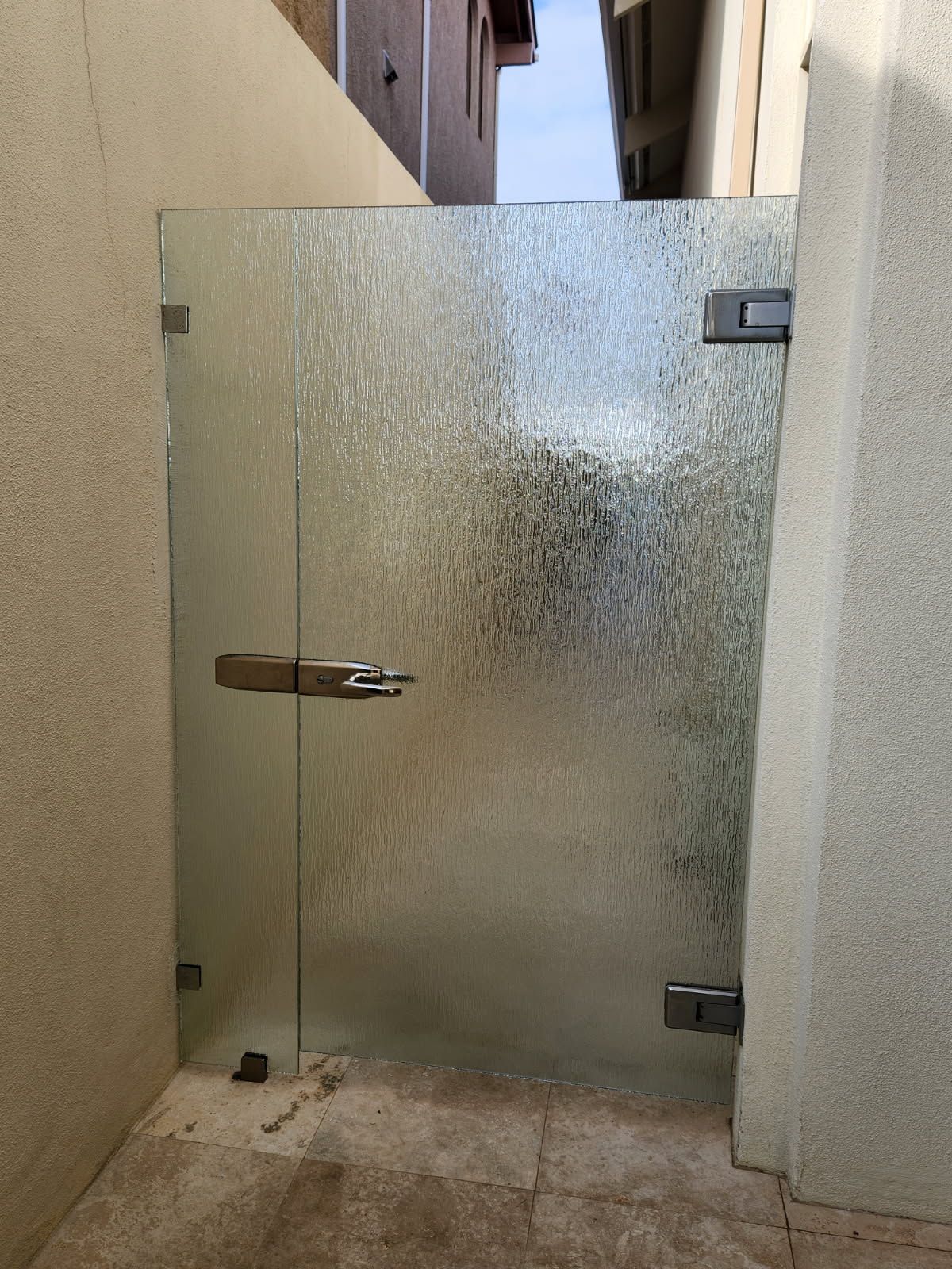 Glass gate with textured surface and metal hardware between concrete walls.