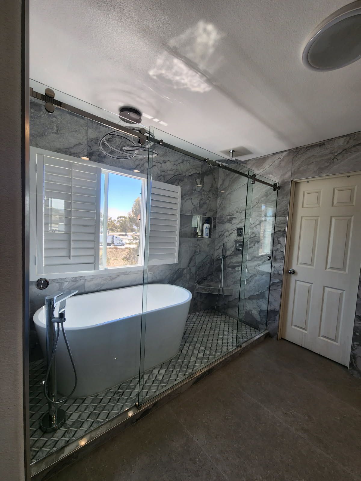 Luxurious bathroom with a glass-enclosed shower, soaking tub, window with shutters, and stone tile walls.