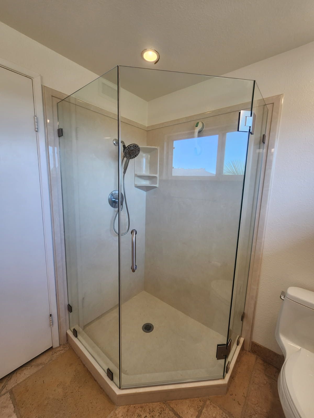 Glass-enclosed shower with beige walls, a window, and a white toilet.