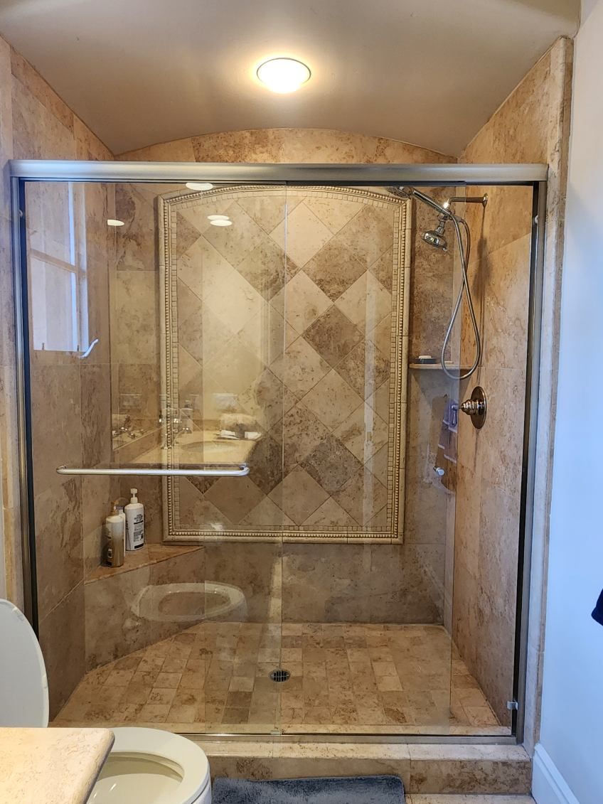 Shower with glass doors and beige tile, a handheld showerhead, and a soap dispenser.