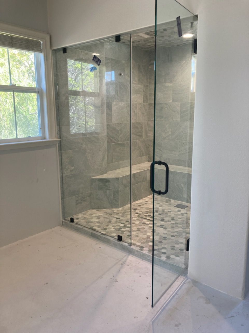 Glass shower with door and window to the left, stone floor and tile wall. Black door handle and hinges.