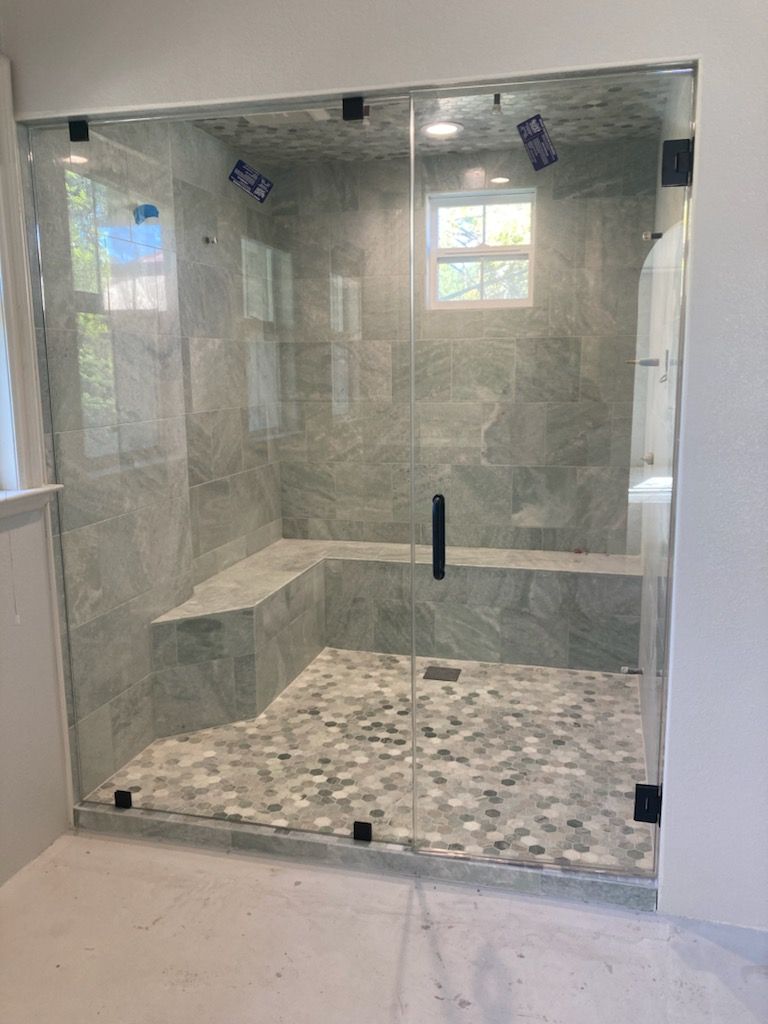 Glass shower enclosure with gray tile walls, a built-in bench, and pebble floor.