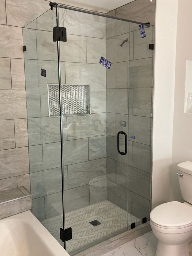 Glass shower enclosure with black hardware, set against gray tiled walls, next to a white toilet.