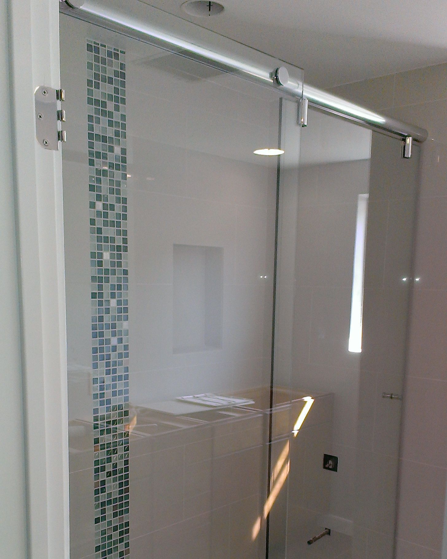Glass shower door with sliding mechanism and tiled accent wall.