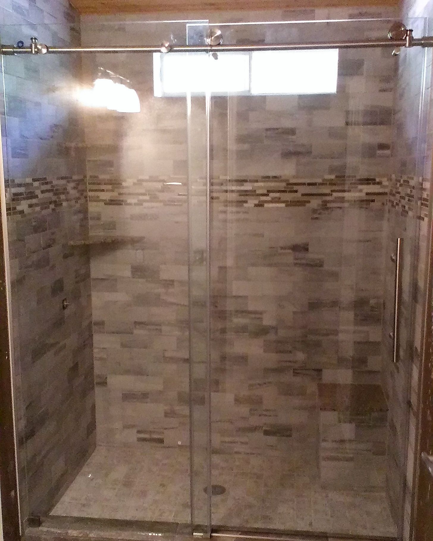 Glass shower enclosure with sliding door, tiled walls, and small window.