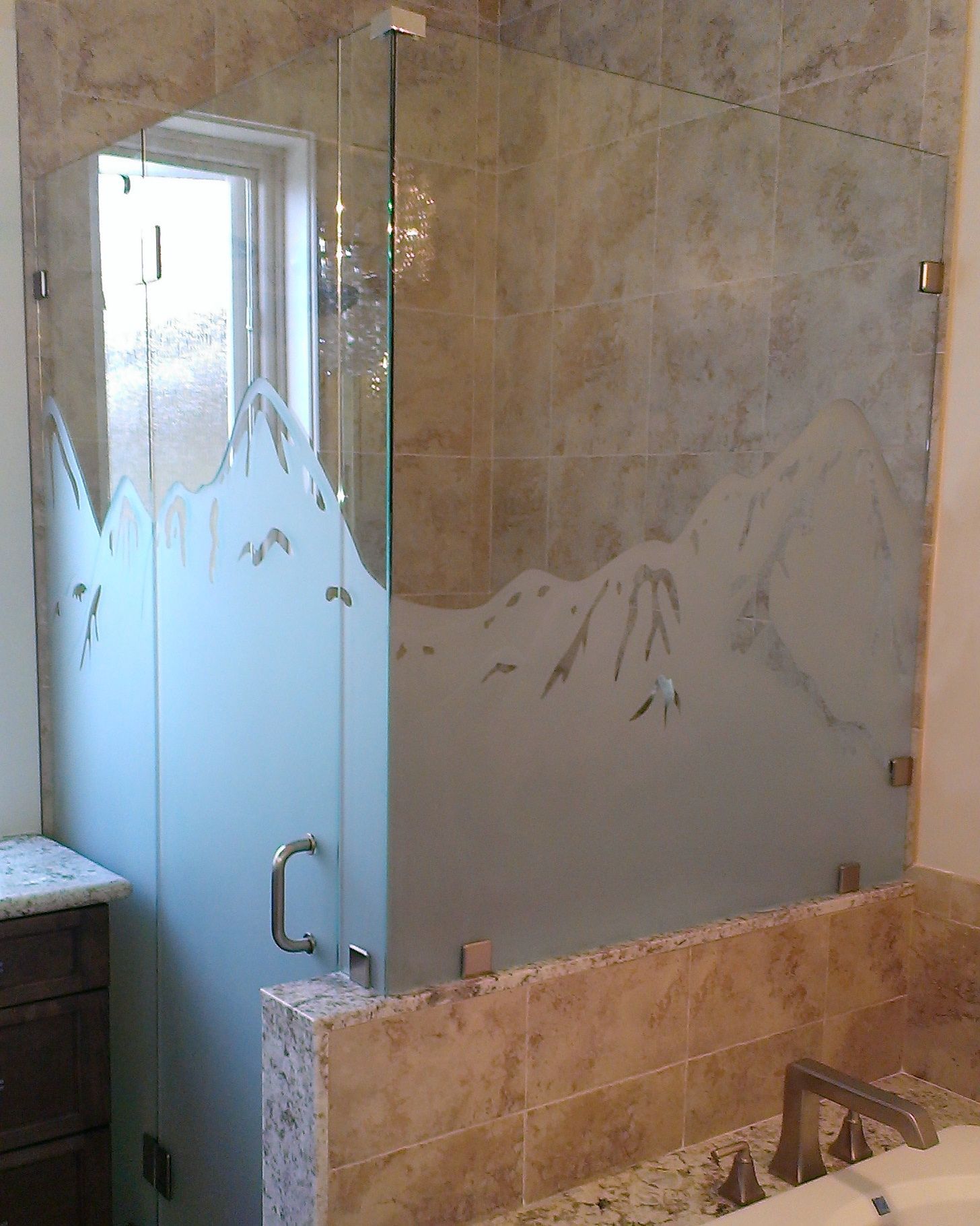 Glass shower enclosure with frosted mountain design; set against beige tile.