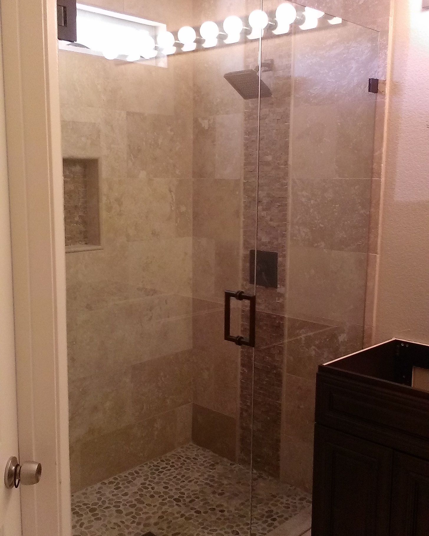 Glass shower enclosure with stone tile walls, pebble floor, and dark cabinet.