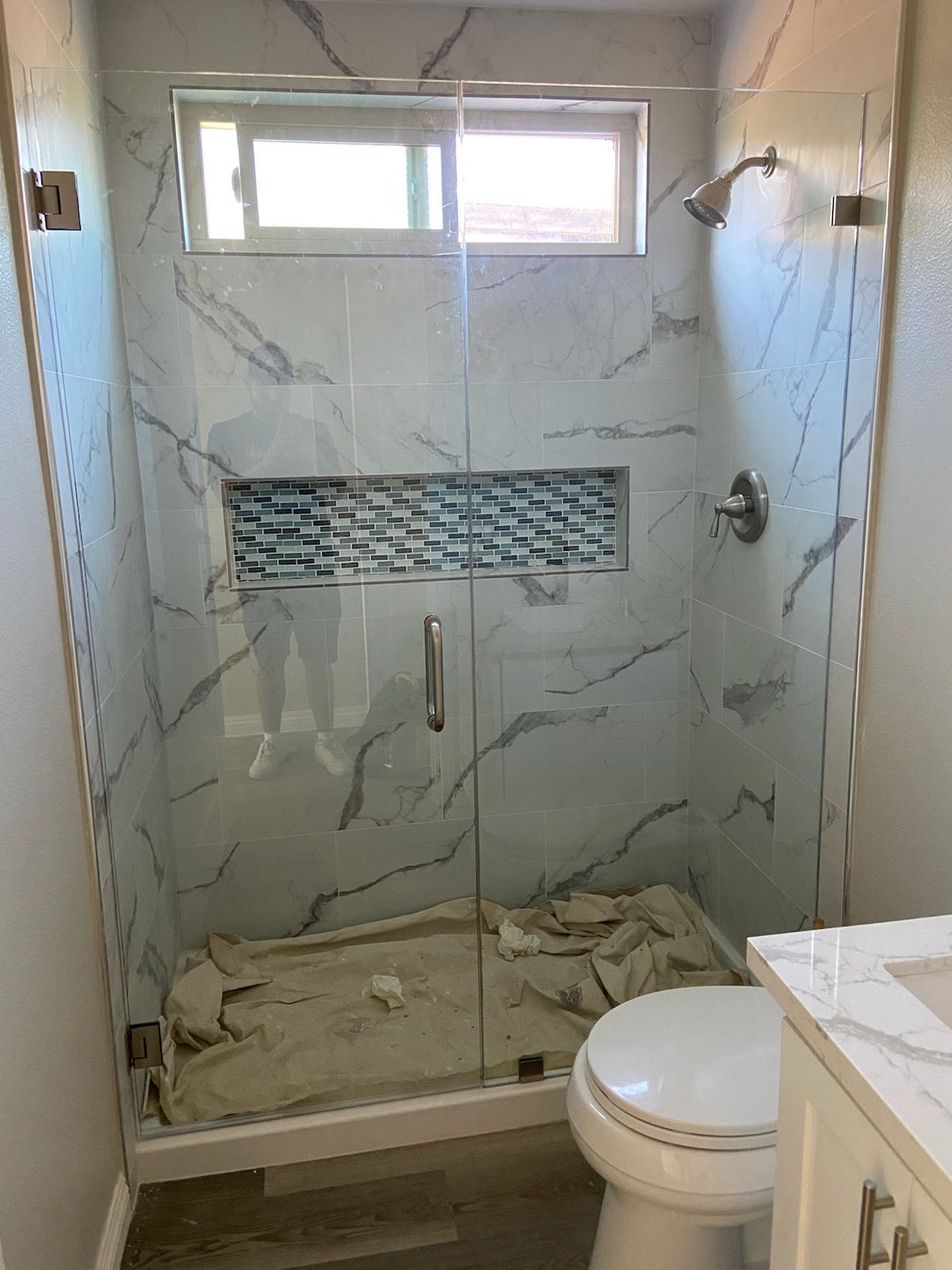 Shower stall with glass doors, marble-patterned tile, blue mosaic accent, and toilet in front.