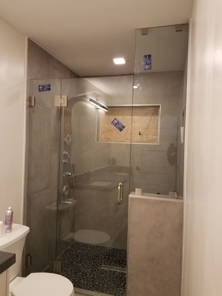 Glass shower enclosure with gray tile, pebble floor, and white toilet.