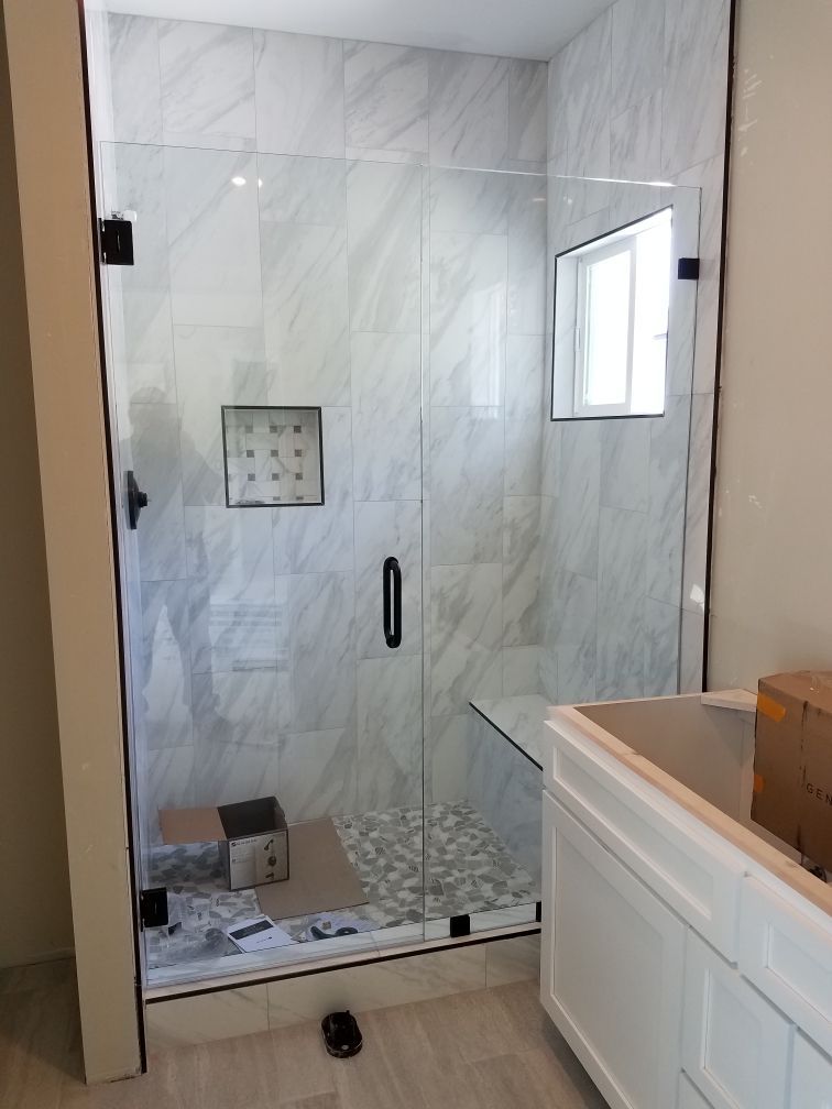 Glass shower enclosure with gray tiled walls and white vanity.