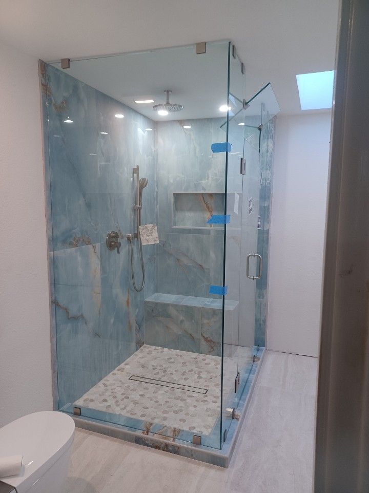 Glass-enclosed shower with blue tile walls, a built-in bench, and a light-colored mosaic floor.
