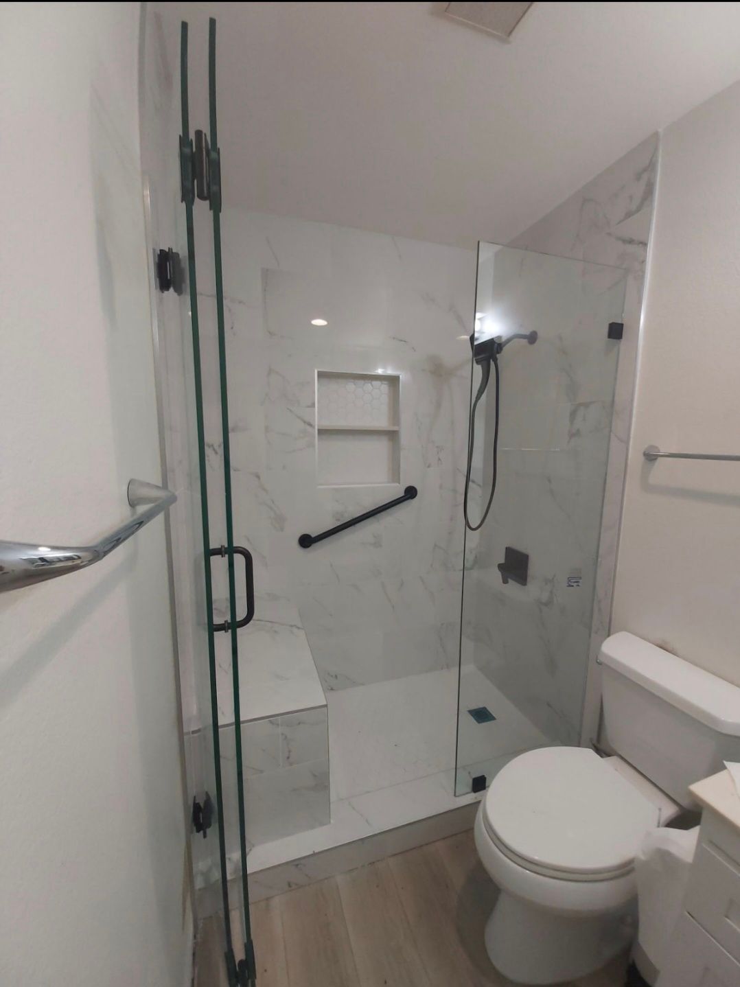Modern bathroom with glass shower door, marble tile walls, a toilet, and a grab bar.