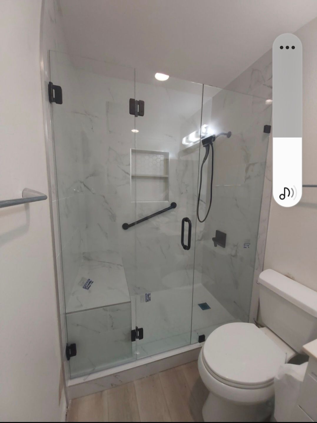 Modern shower with glass doors, white marble tiles, black fixtures, and a toilet.