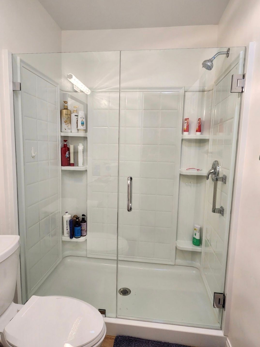 Shower with glass doors and white tile walls, built-in shelves holding toiletries.