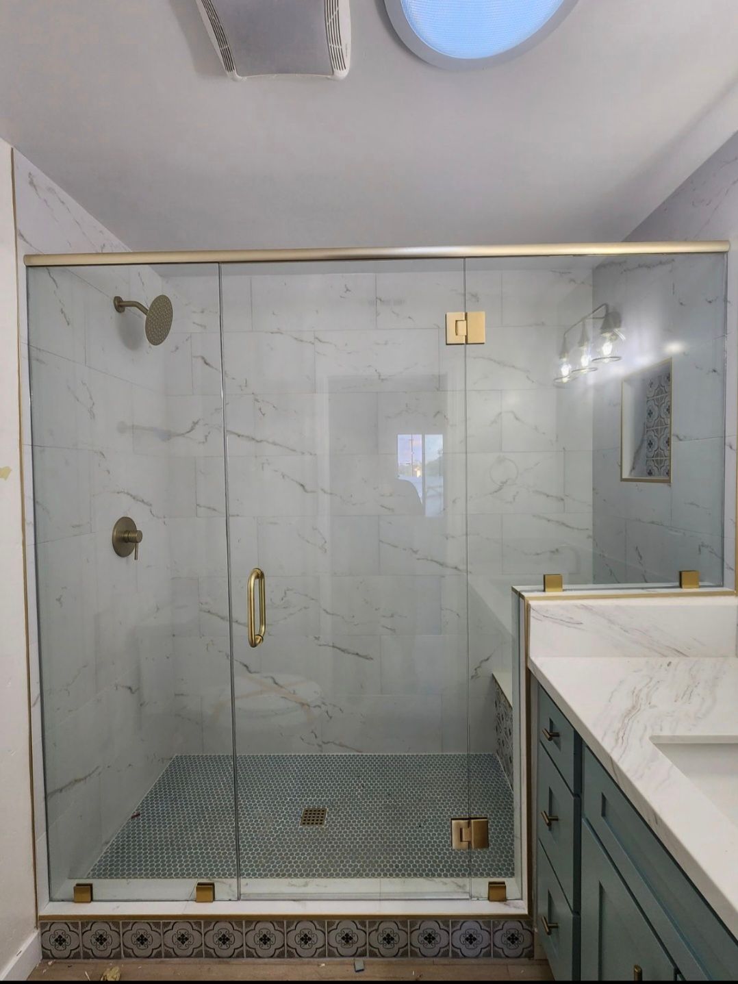 Shower with gold fixtures and marble tile, next to a teal vanity.