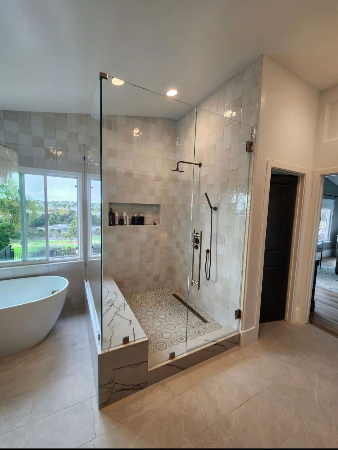 Modern bathroom with glass shower, built-in bench, stone tile, and freestanding tub.
