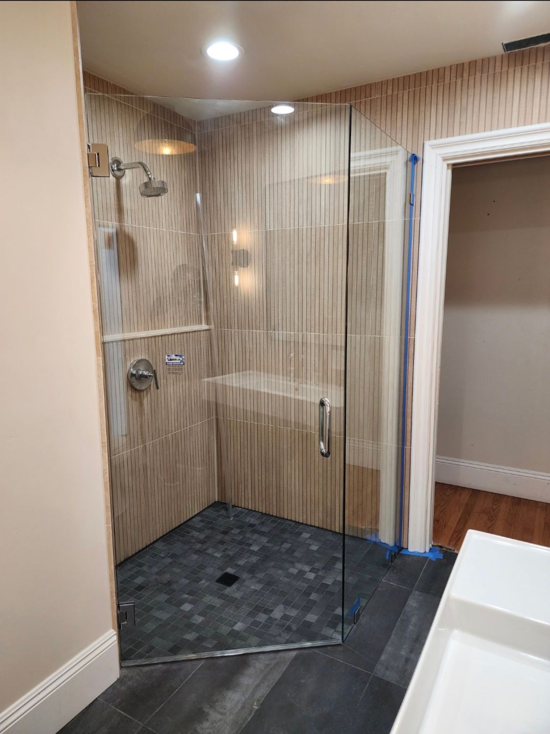 Bathroom with tiled shower stall, glass door, dark floor, and bench.