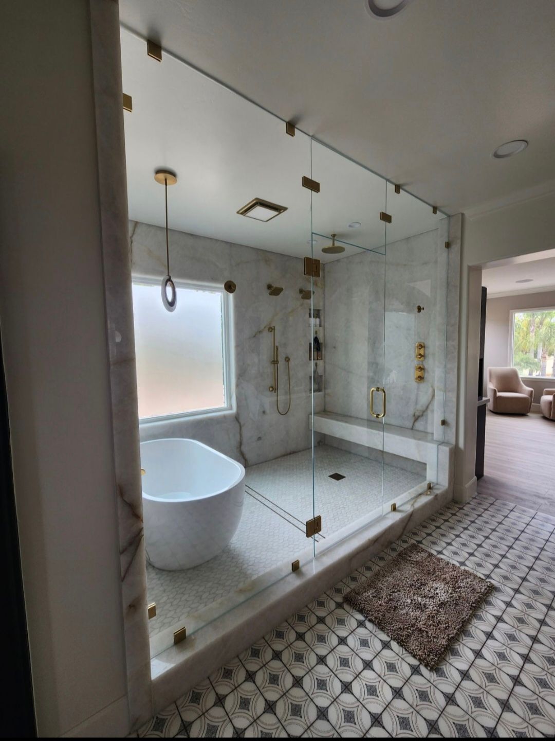 Bathroom with glass shower, soaking tub, marble tile, and gold fixtures.