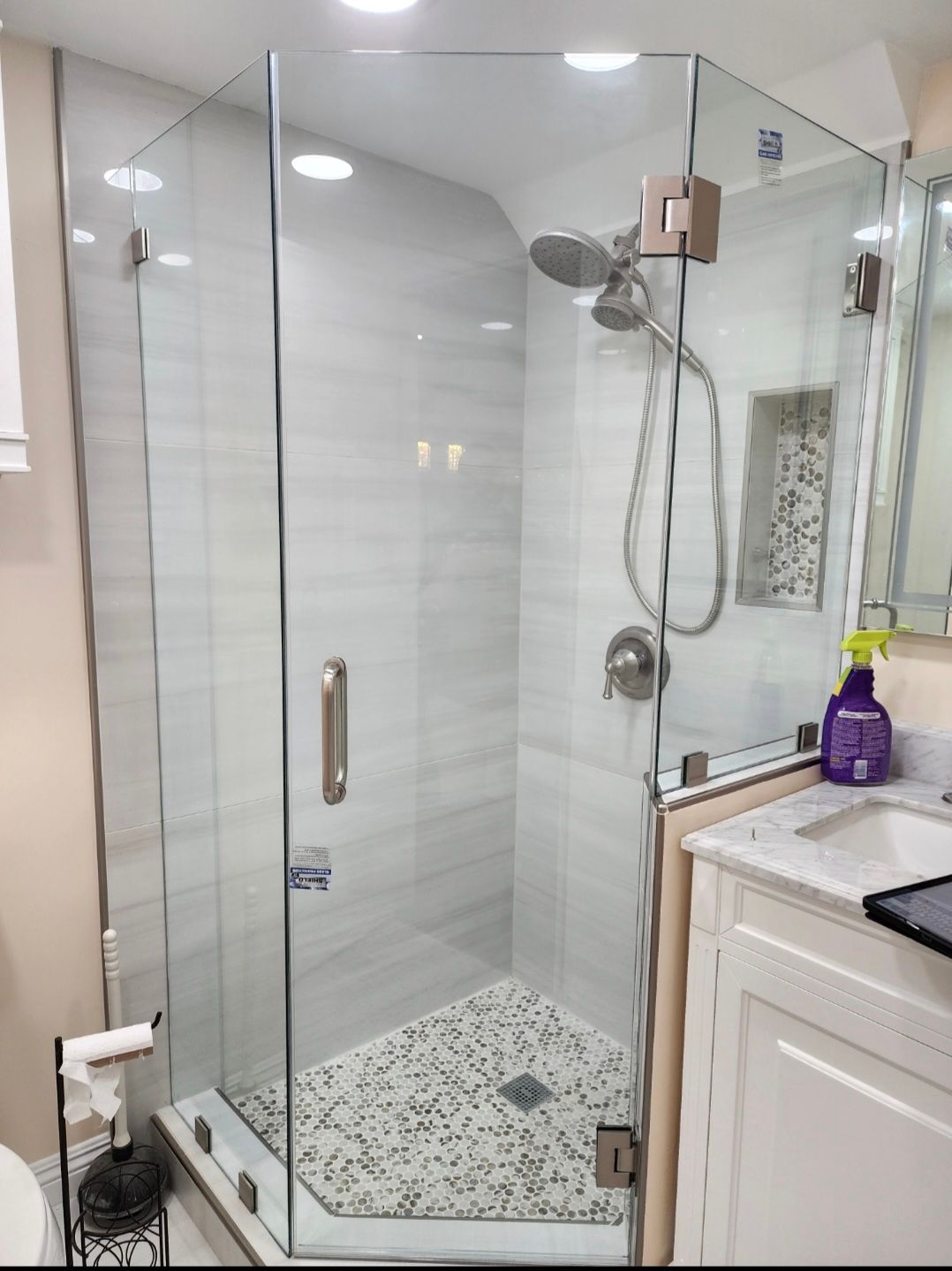 Glass shower enclosure in a bathroom with white tile walls and a gray pebble floor.