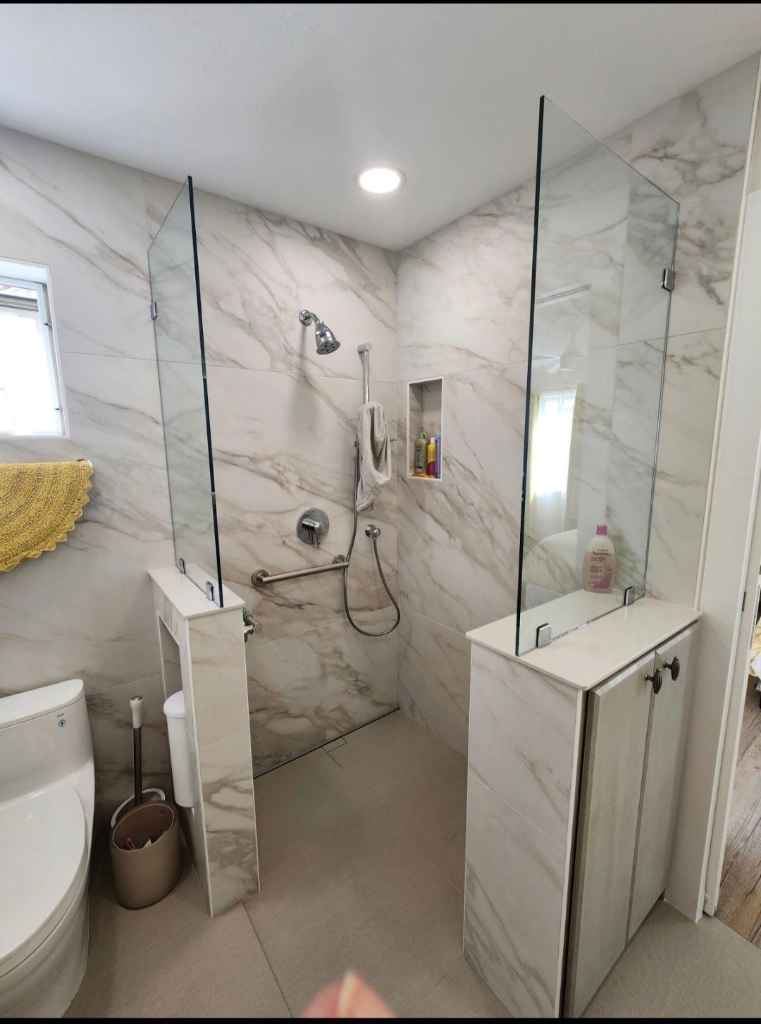 Modern marble-tiled bathroom with glass shower walls and cabinetry, accessible shower fixtures.