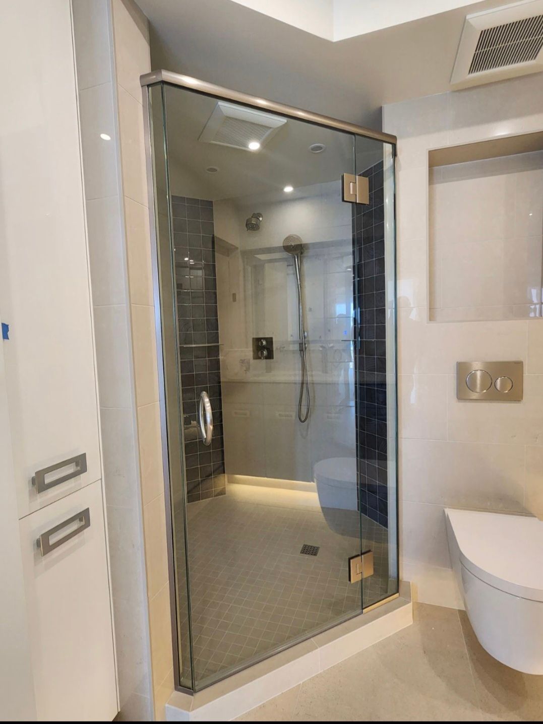 Modern bathroom with glass shower door, white toilet, and recessed wall storage.