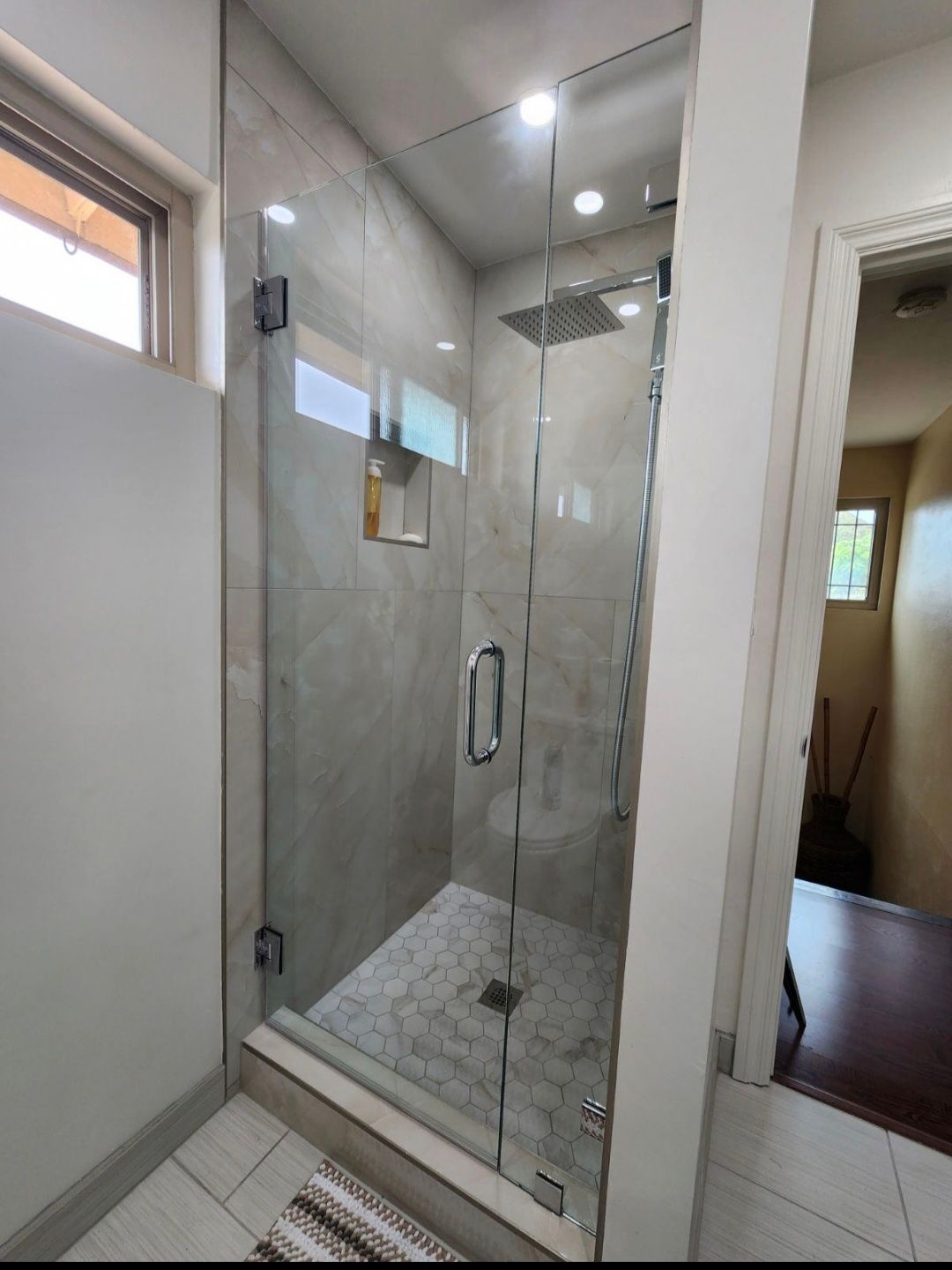 Glass shower enclosure with gray tile, a rain showerhead, and a small window.