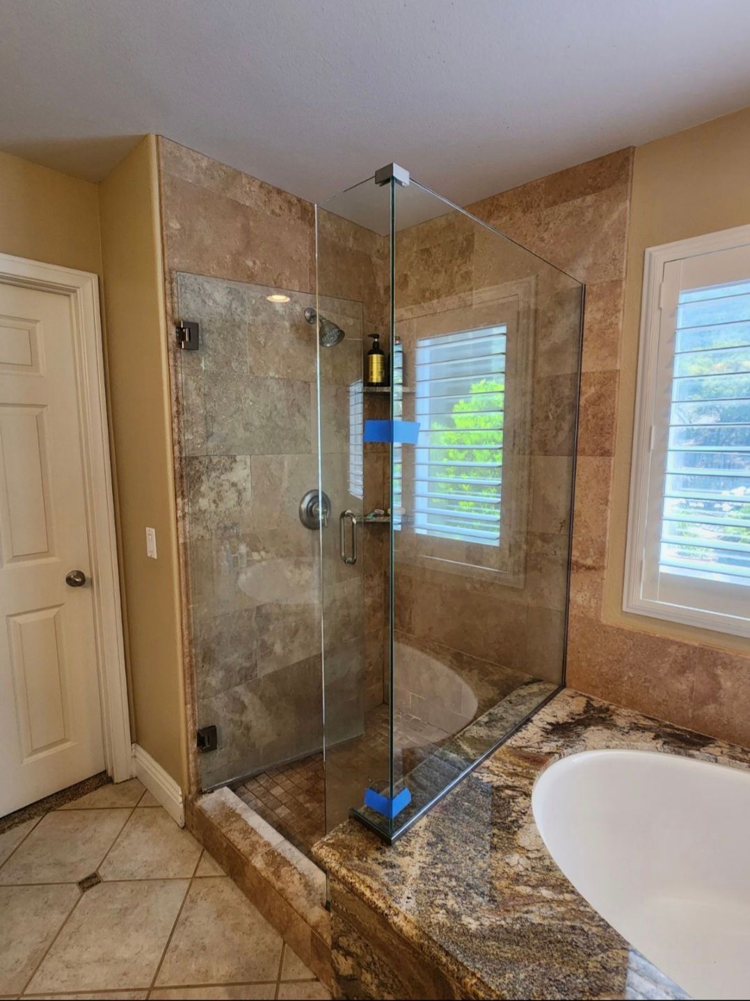 Glass shower enclosure with stone tile walls, next to a window and countertop.