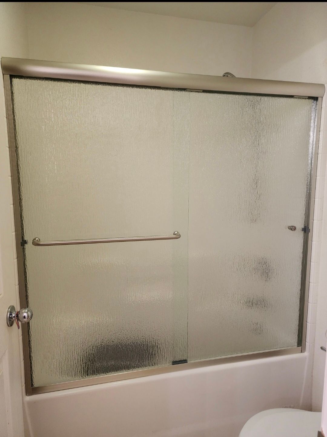 Shower with frosted glass sliding doors, silver frame, and a towel bar above a bathtub.