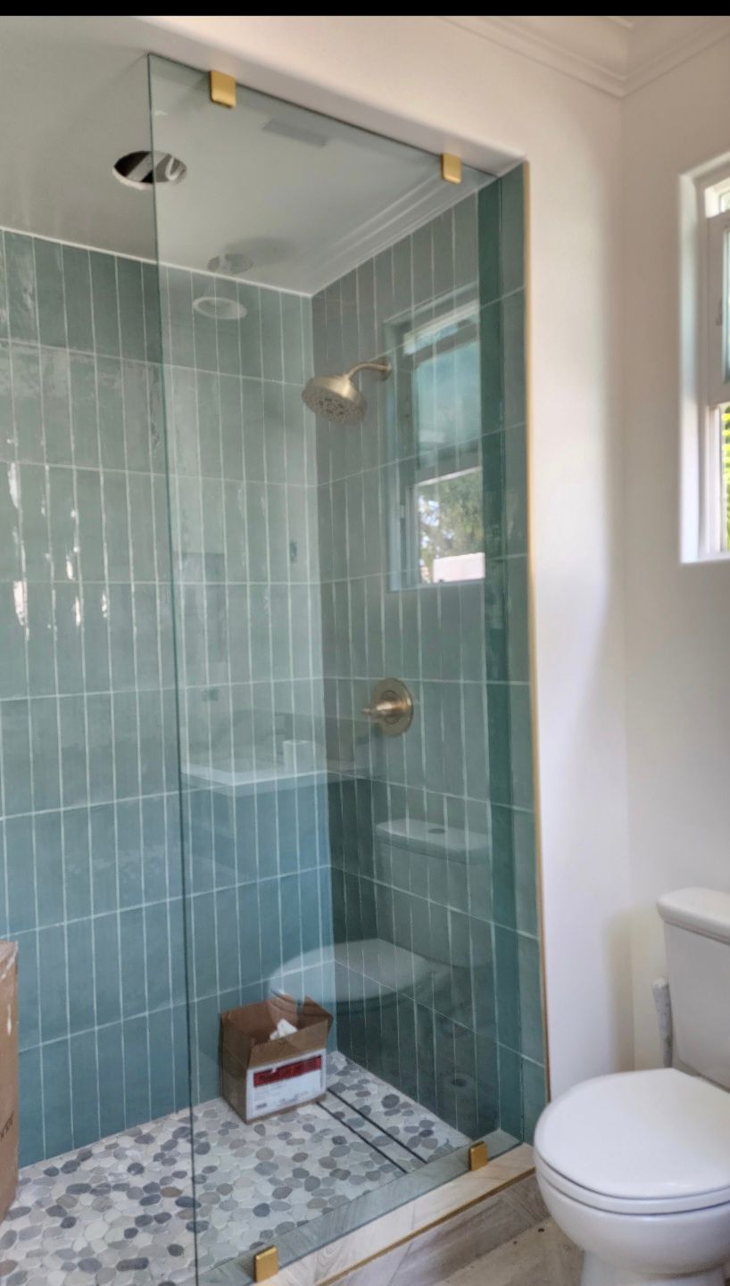 Glass shower with teal tile walls, gold fixtures, and a white toilet.