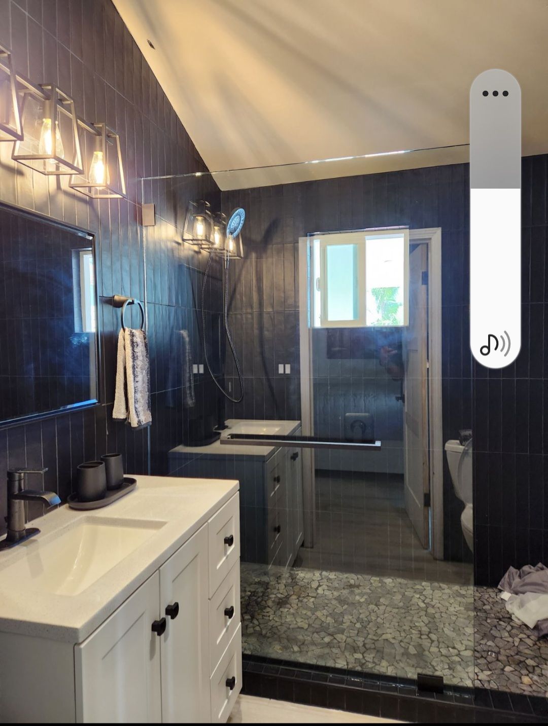 Bathroom with dark blue tiled walls, white vanity, glass shower, and open doorway.