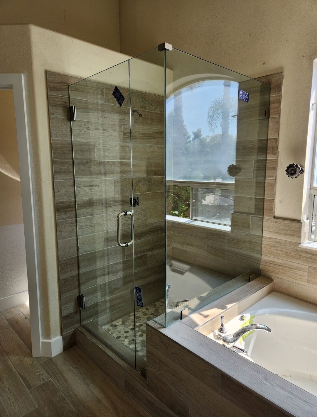 Frameless glass shower with stone tile walls, next to a bathtub.