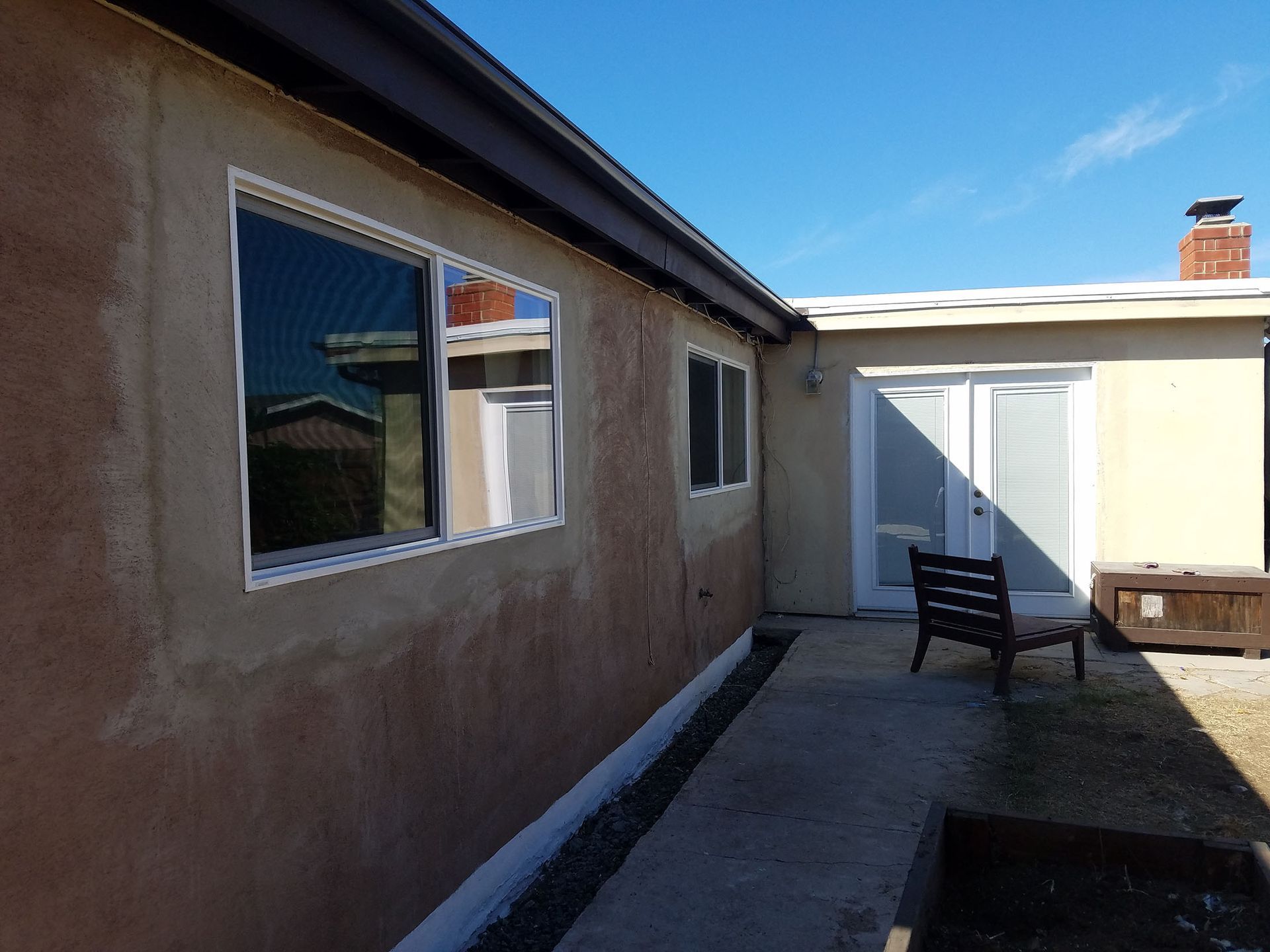 Exterior of a home with stucco walls, windows, and a pathway leading to a sliding glass door.