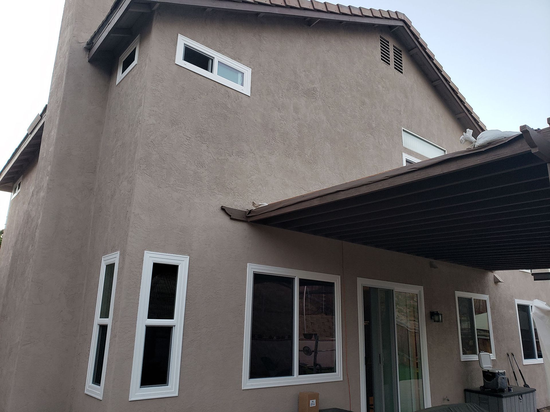 Tan stucco house exterior with white-trimmed windows and a brown pergola.