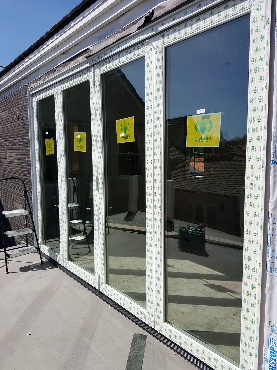 White framed glass doors, partially installed on a building. Yellow safety stickers are visible.