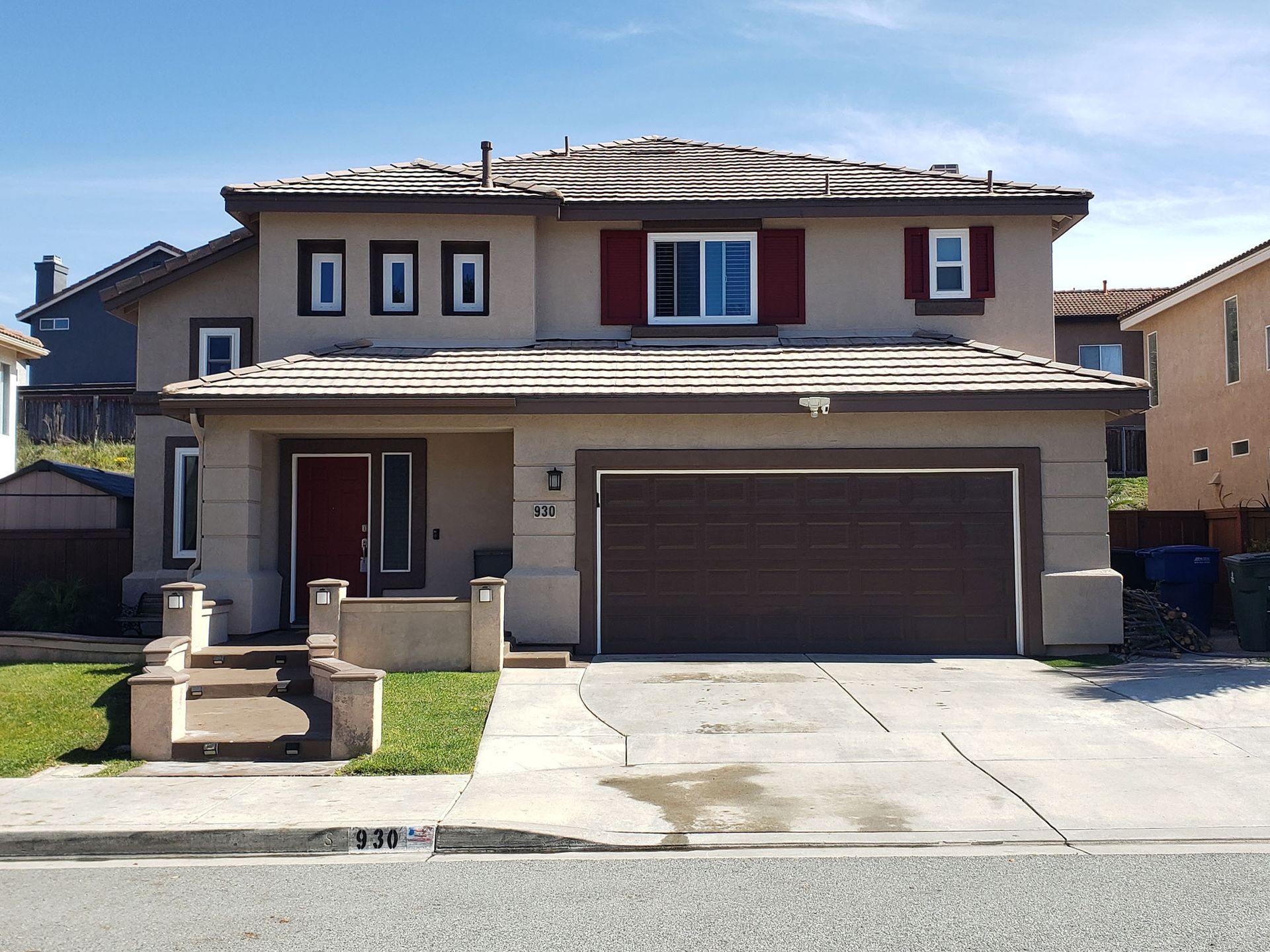 Two-story beige house with a brown garage door and red accents; gray driveway.