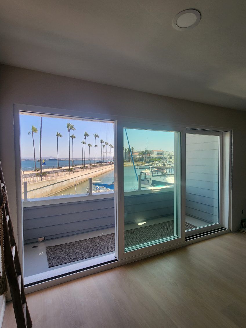 Interior view of three large windows overlooking a waterfront with palm trees and boats.