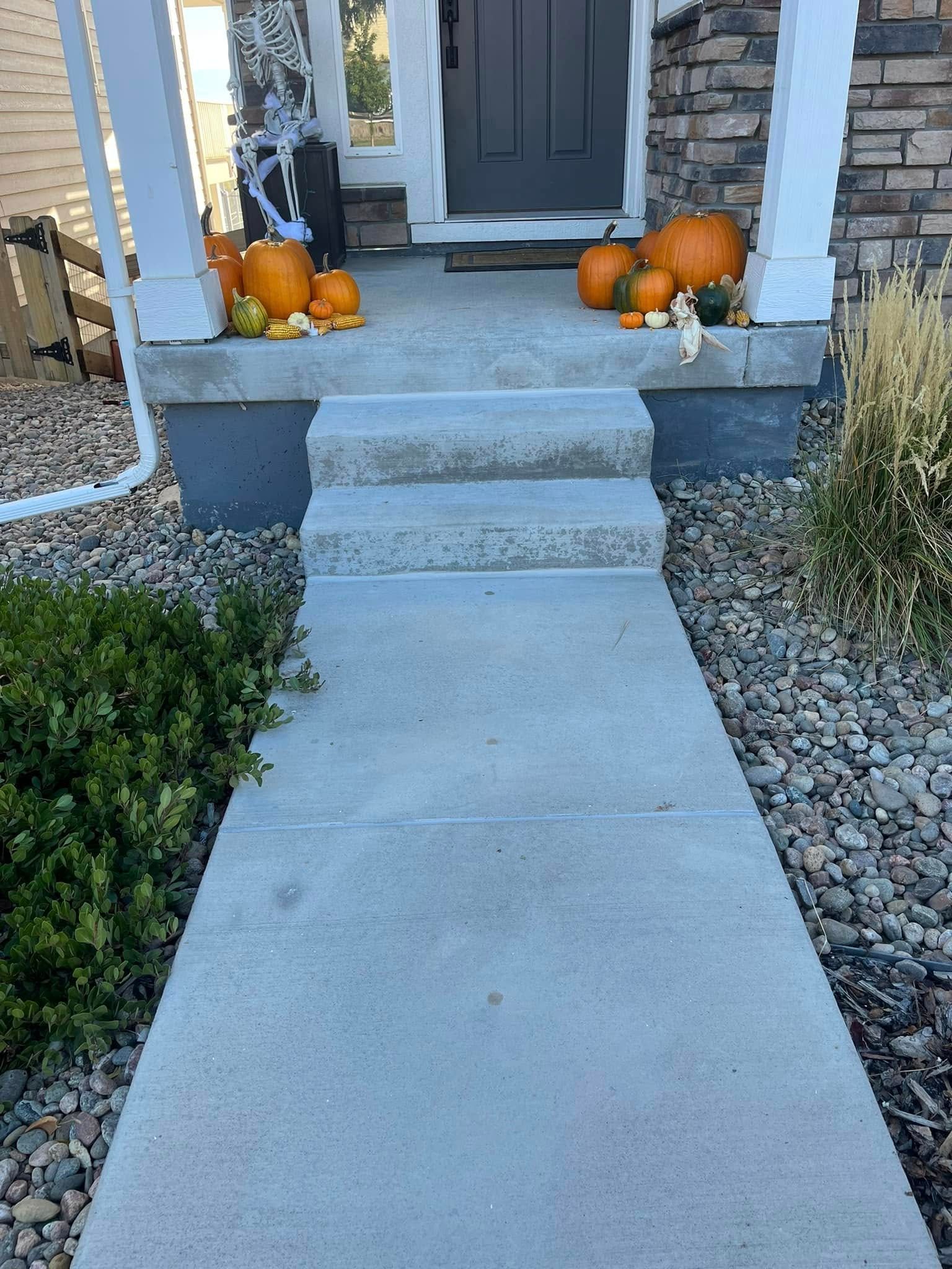 A concrete walkway leading to a porch decorated for halloween with pumpkins.