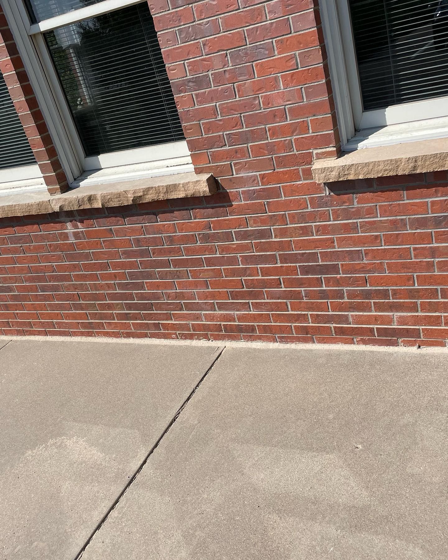 A brick wall with two windows and a concrete sidewalk in front of it.