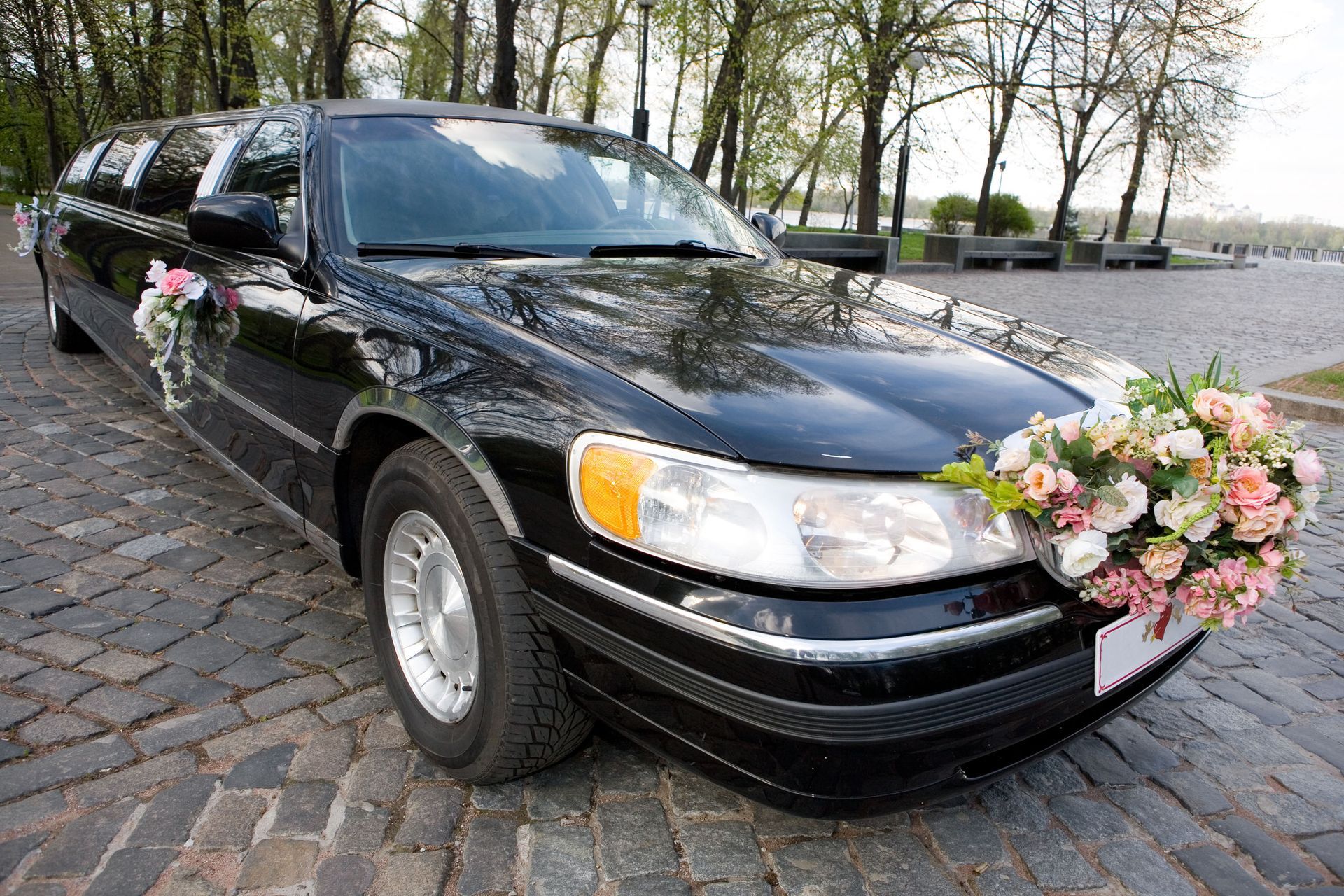 Black limousine decorated with pink and white flowers, parked on a cobblestone street.