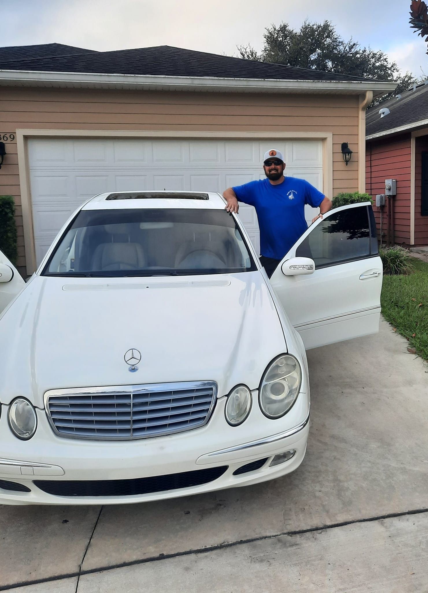 A man is standing next to a white car in front of a garage door.