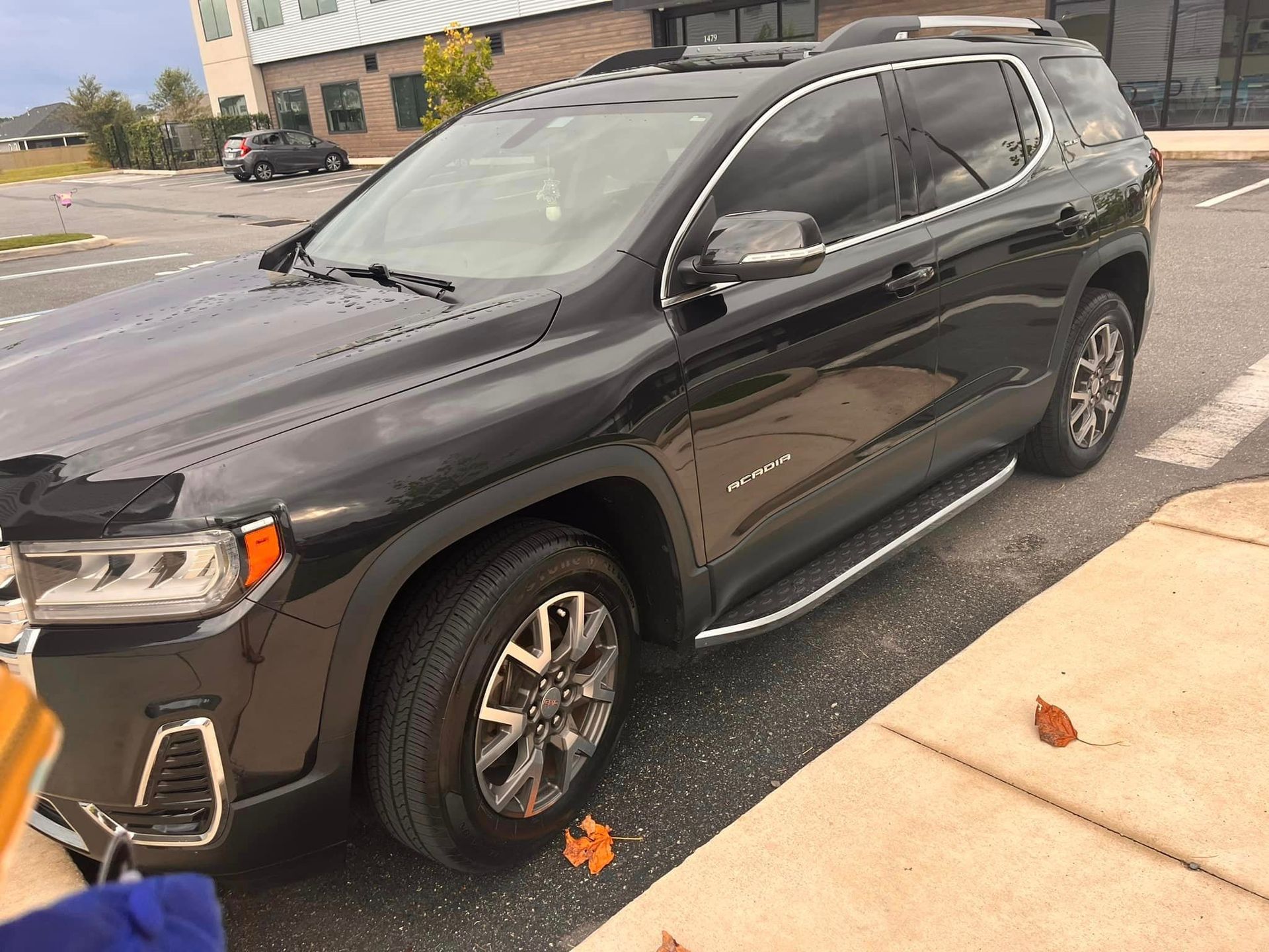 A black suv is parked in a parking lot next to a sidewalk.