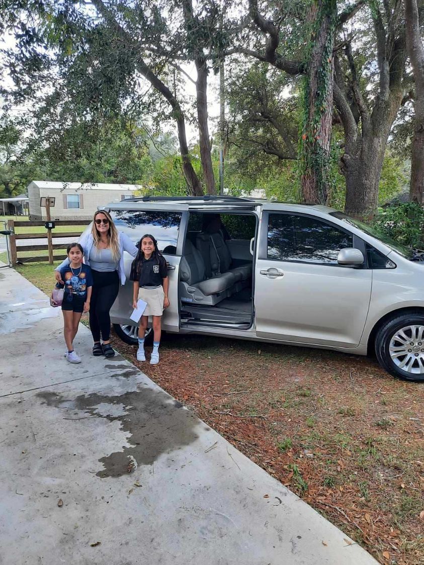 A woman and two children are standing in front of a minivan.