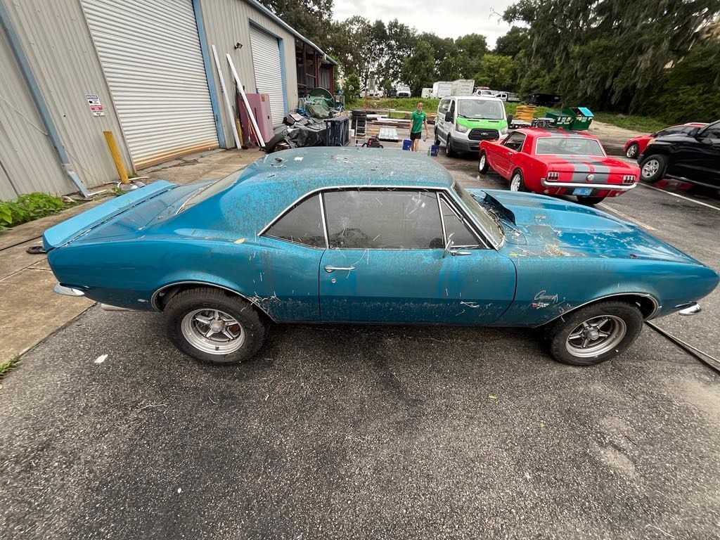 A blue car is parked in a parking lot next to a building.