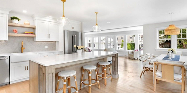 A kitchen with white cabinets , a large island , stools and a dining room.