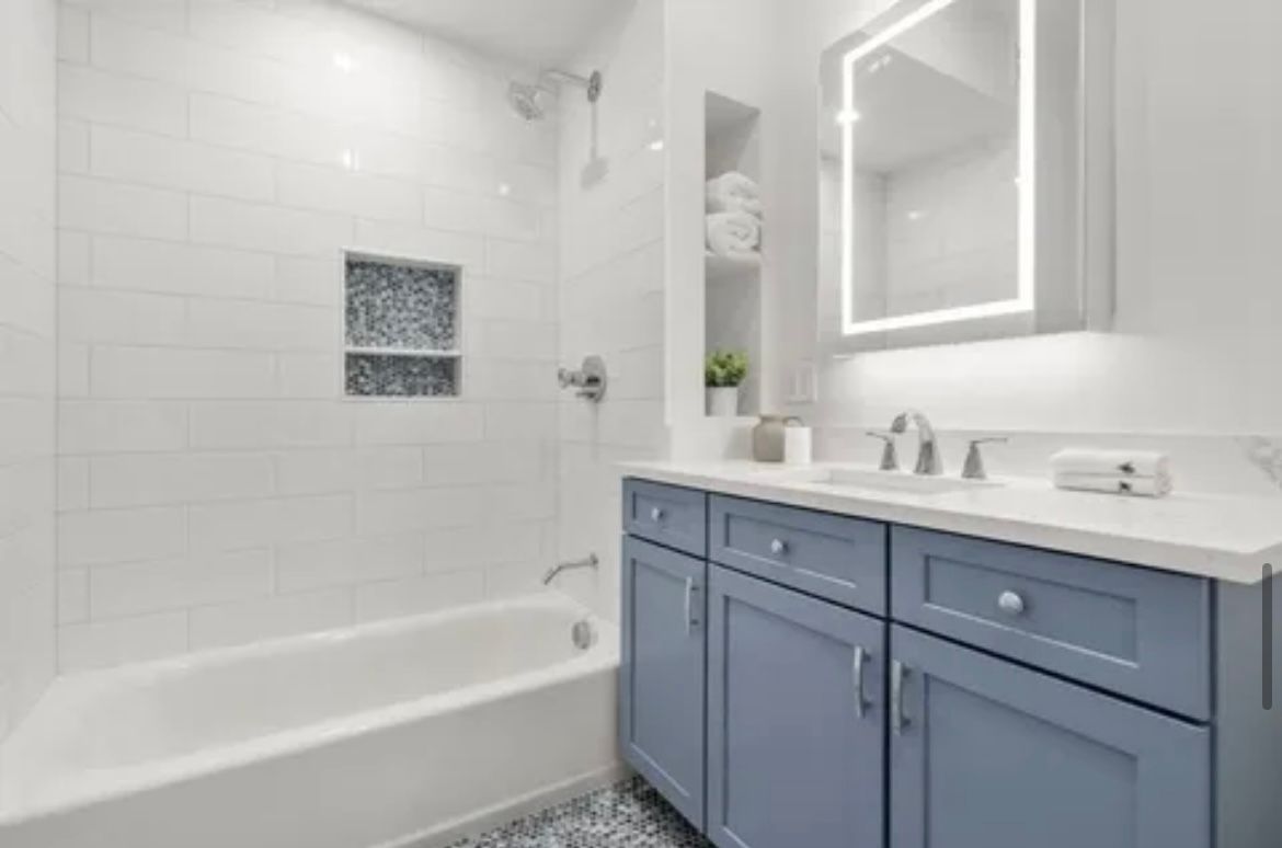 A bathroom with blue cabinets, a bathtub, a sink and a mirror.
