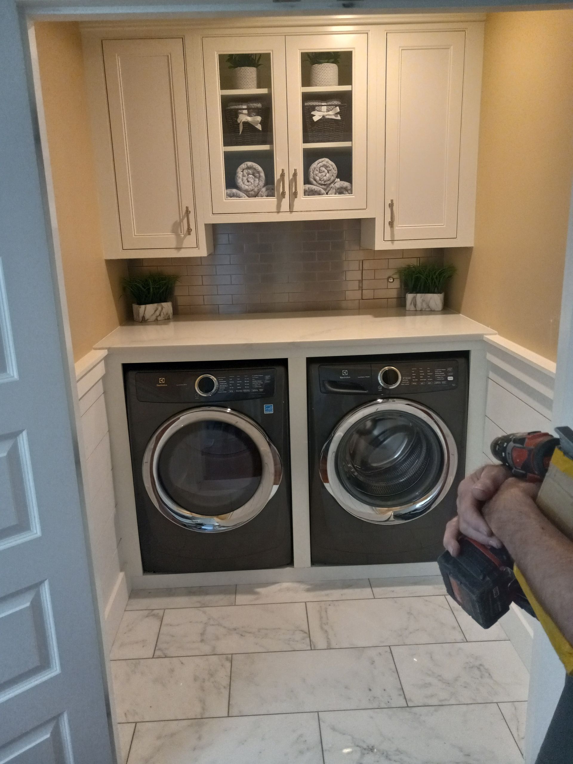 A man is standing in a laundry room with two washers and dryers.