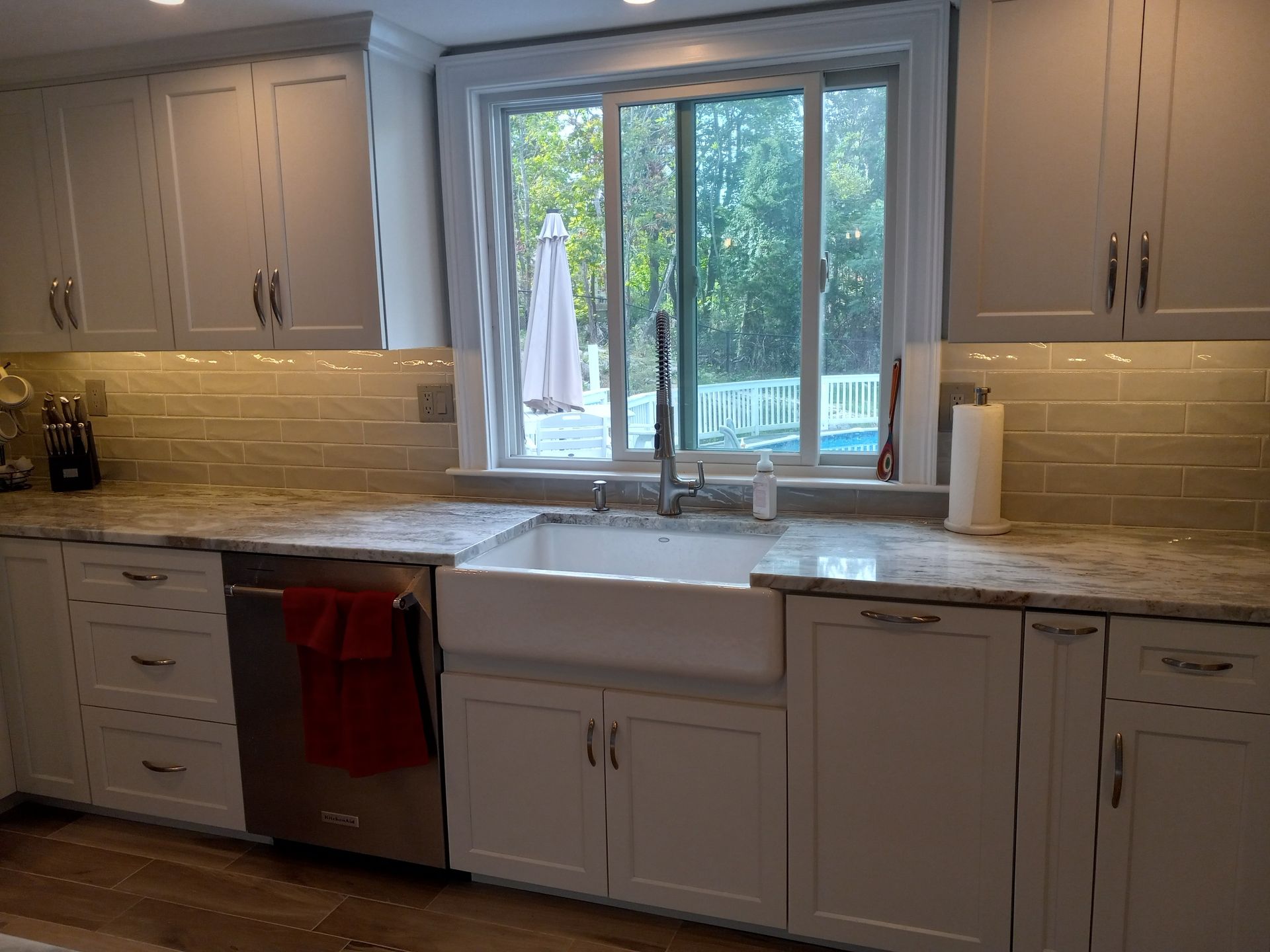 A kitchen with white cabinets, a sink, a dishwasher, and a window.