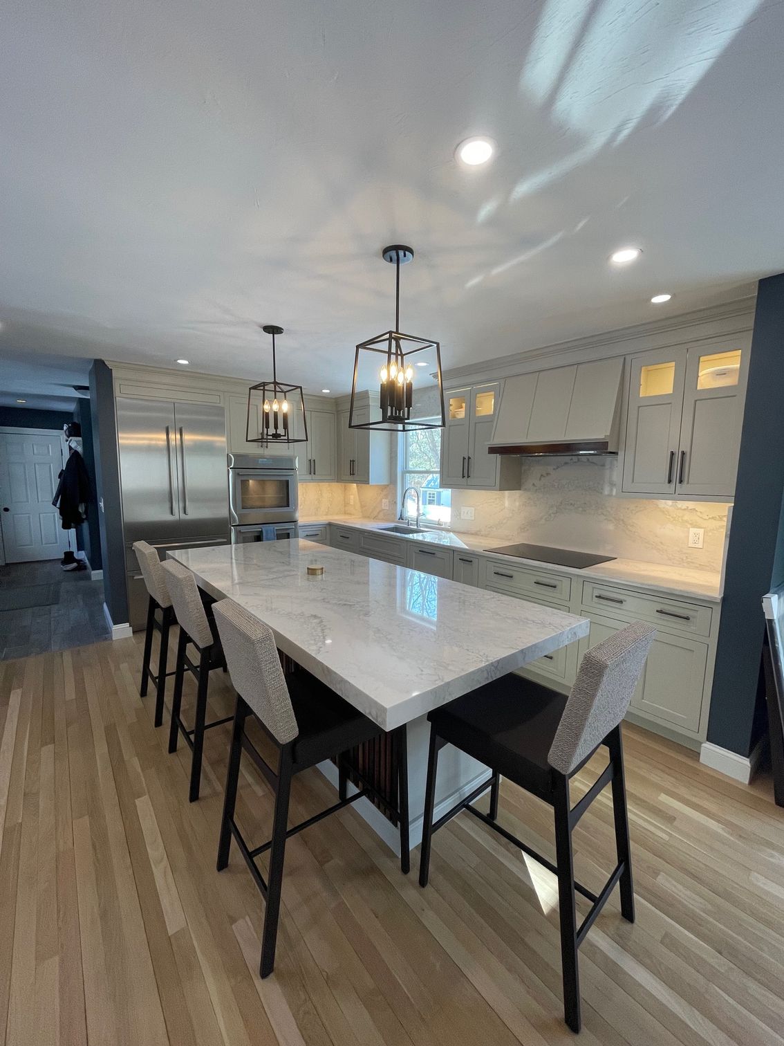 Modern kitchen with large island, pendant lights, bar stools, and light wood flooring.