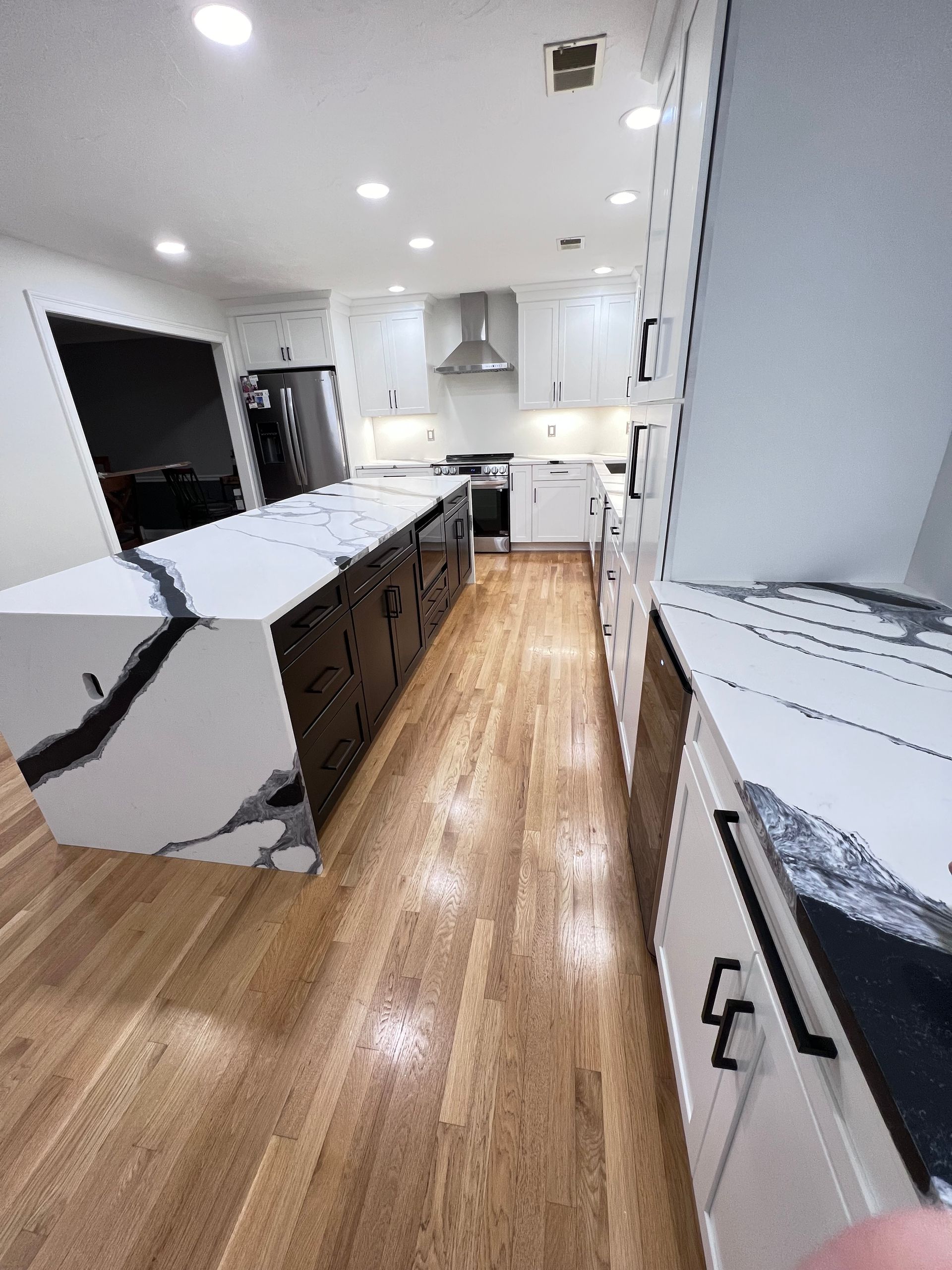A kitchen with white cabinets and hardwood floors and a large island.